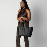 Model holding black daely tote in all brown outfit